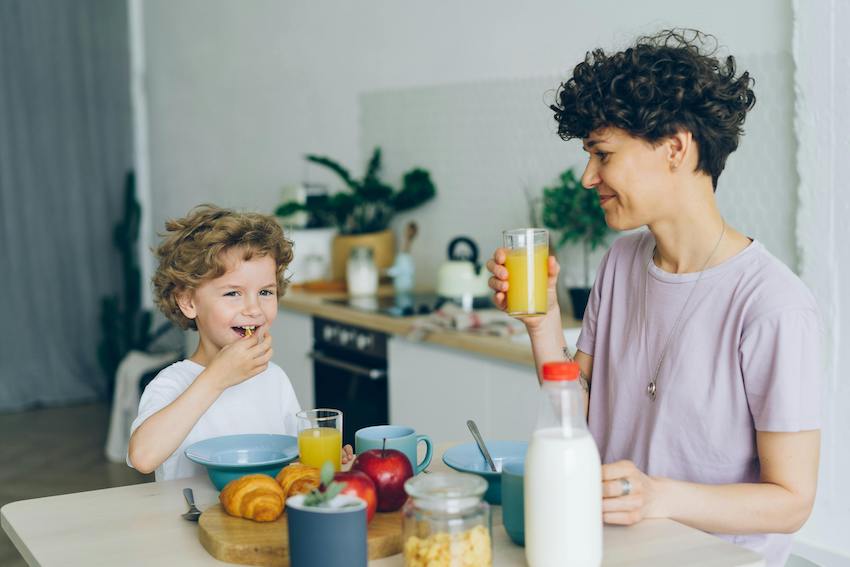 Happy parent and child siting together at the kitchen table eating breakfast. 